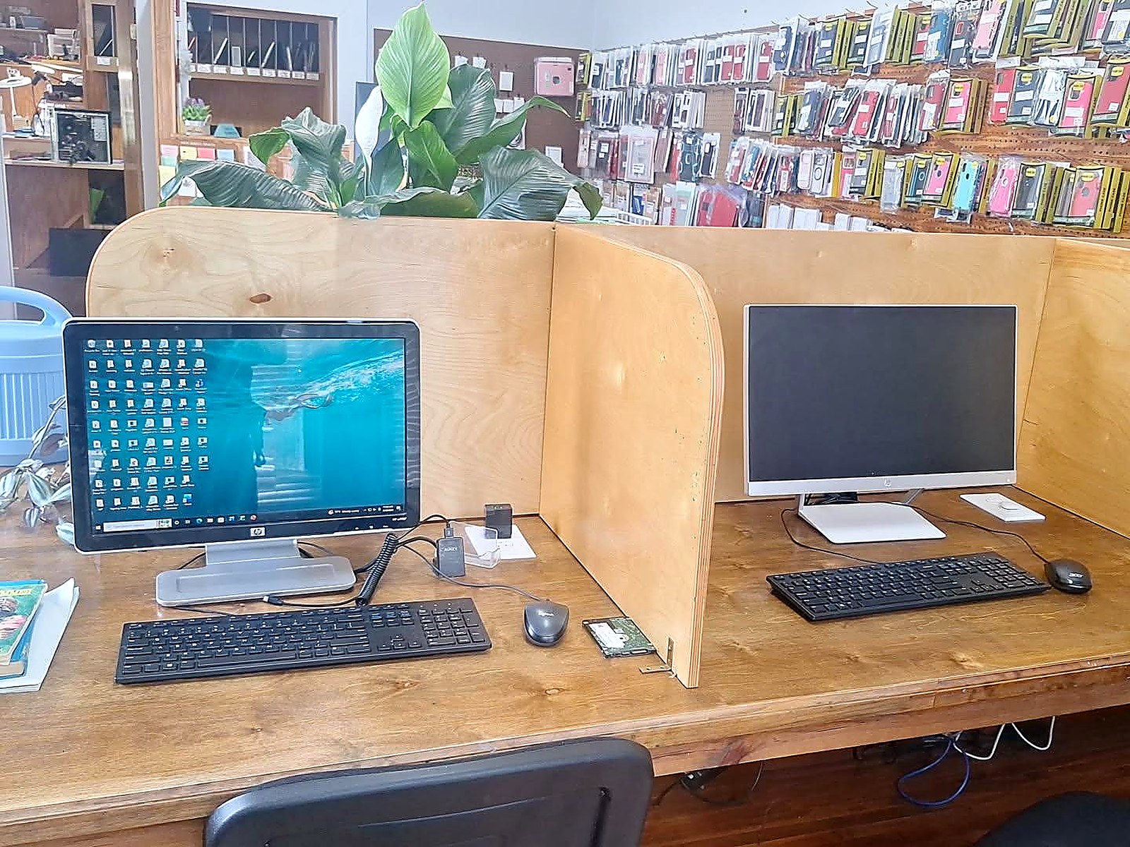 Two public-use computer stations with monitors, keyboards and mice on a wooden counter beside the phone case wall inside Schmidt Sales & Service in Macon, MS