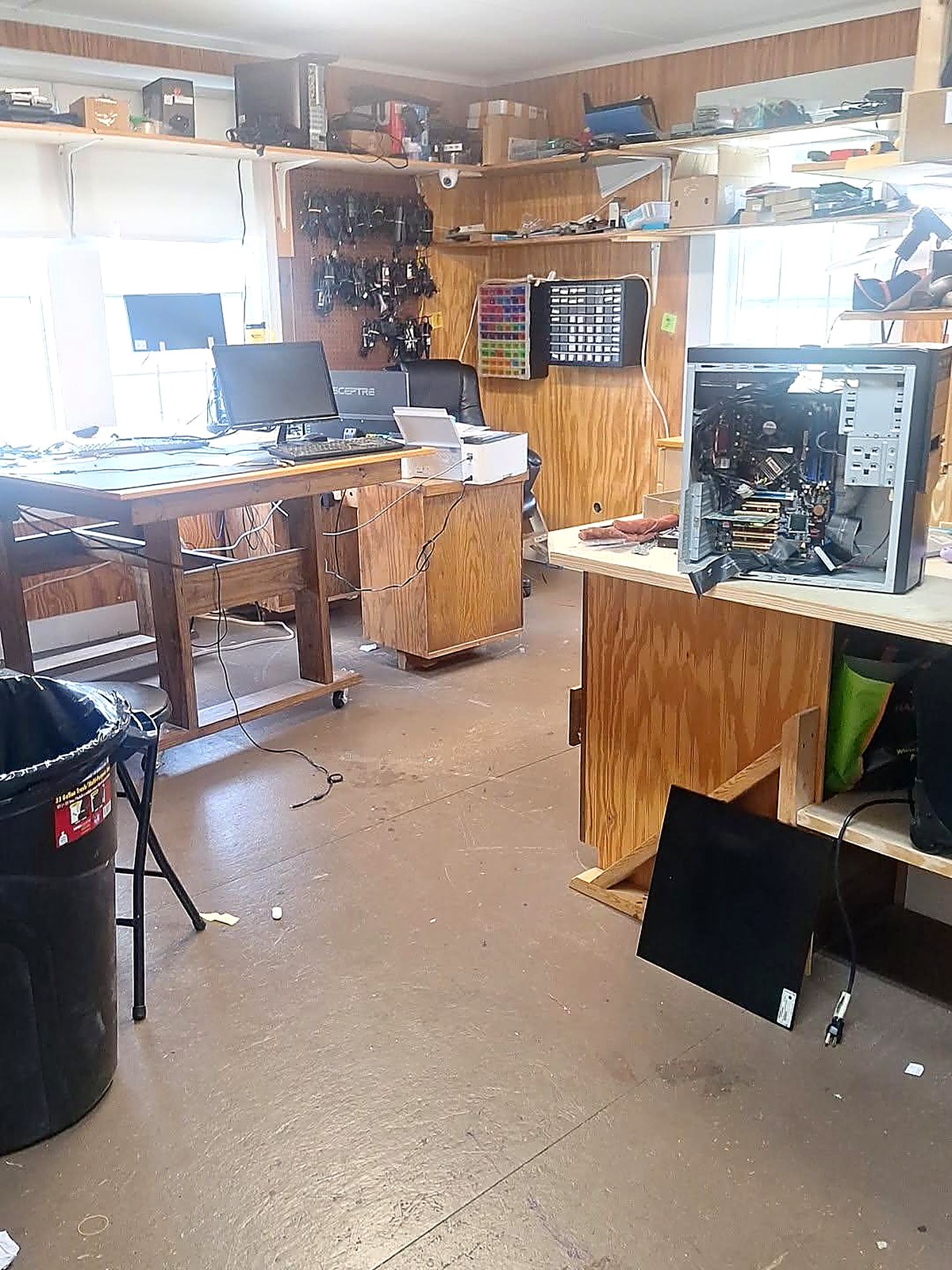 Repair workshop interior with an open desktop computer tower on the bench, cable racks, parts bins and a diagnostics monitor at Schmidt Sales & Service